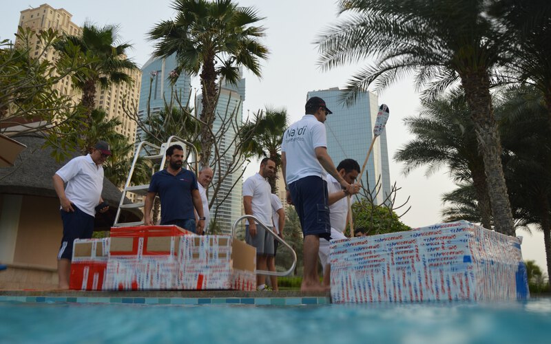 A team carrying the cardboard boats they built to the water, with the Dubai skyline behind