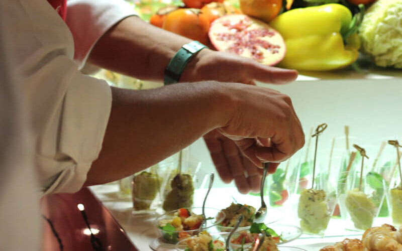 Hands plating finger food, skewers and small glasses lined up along the table