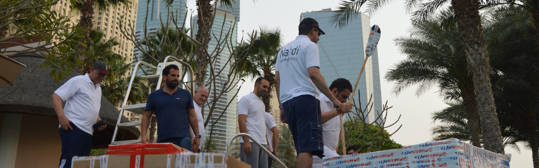 A team carrying the cardboard boats they built to the water, with the Dubai skyline behind