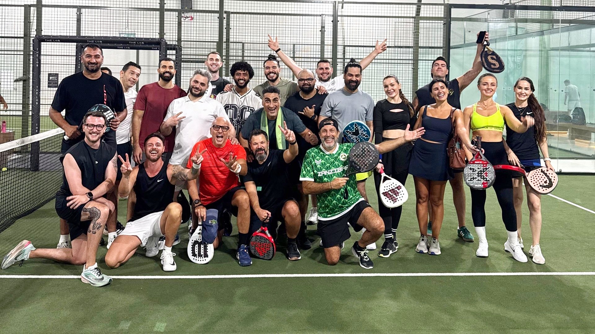 A large group posing together with their rackets on an indoor padel court