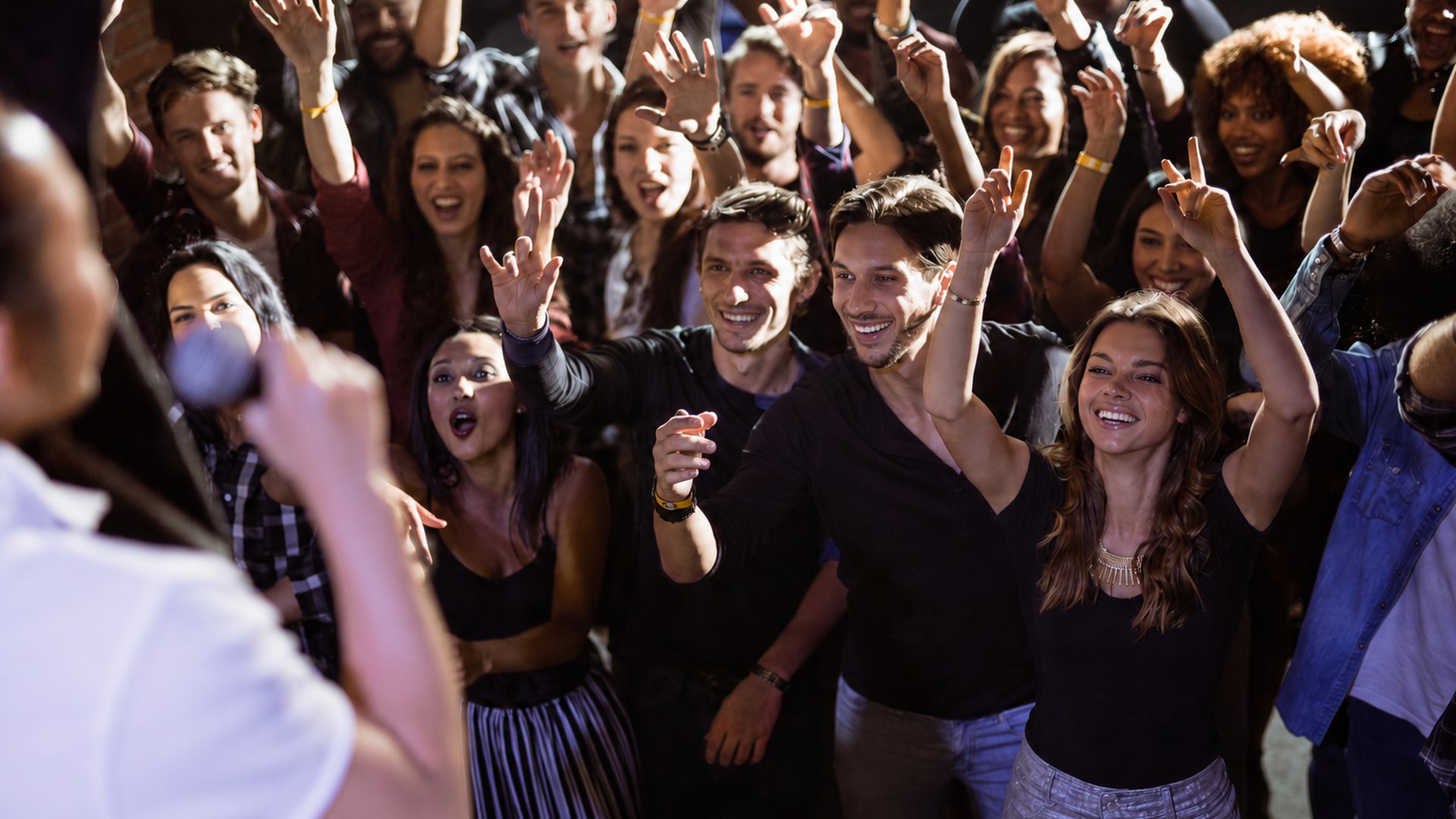 A crowd with their arms raised, cheering and laughing together