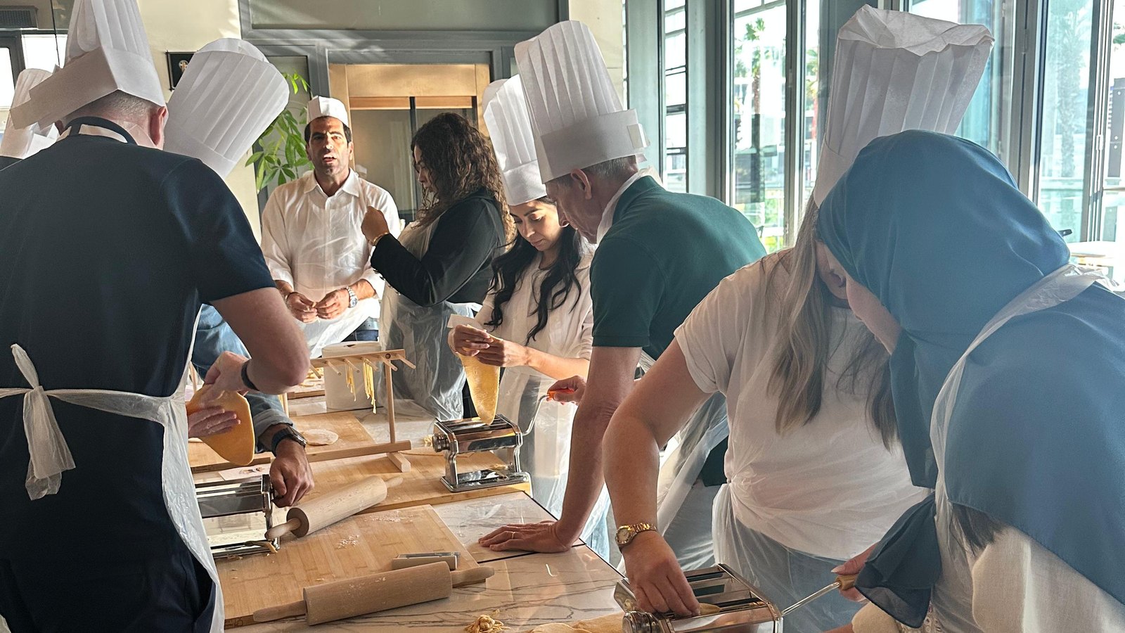 A team working fresh pasta through hand rollers along a long marble table