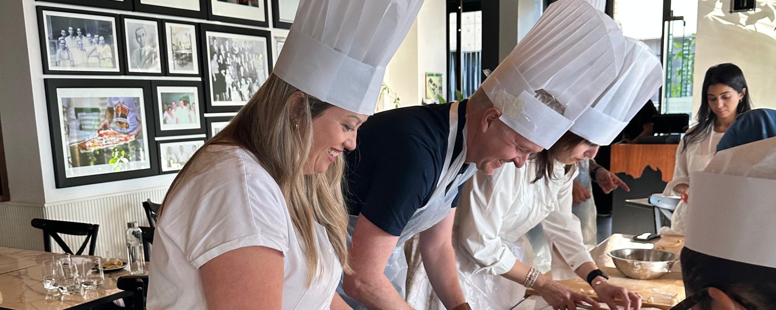 A team in chef hats working the dough side by side along a long table