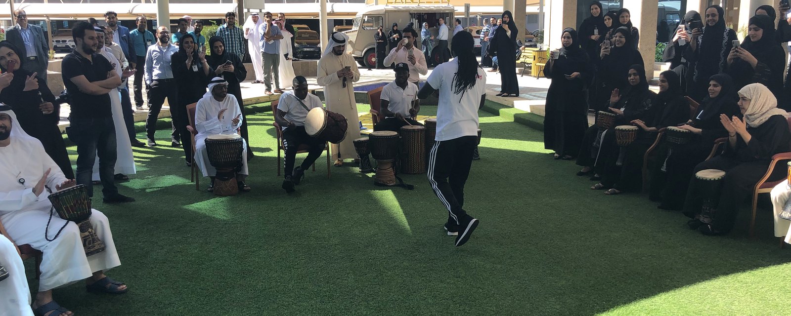 Participants in kandura and abaya playing hand drums together outdoors